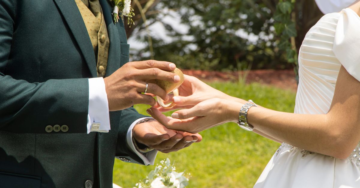 Bride and groom exchanging rings in an elegant outdoor wedding ceremony.